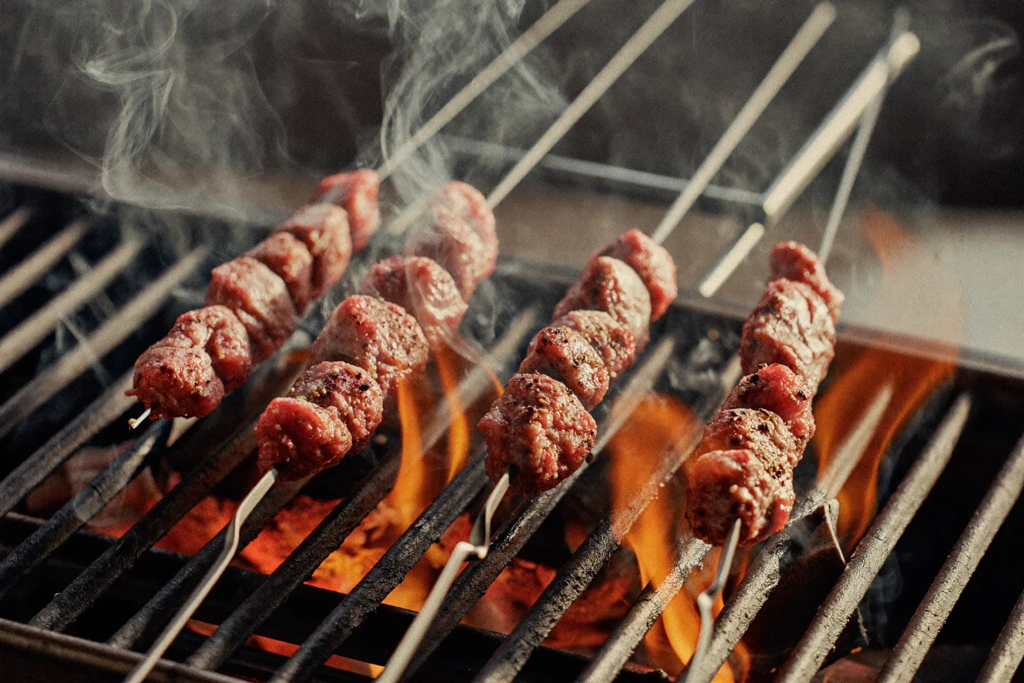 Adana skewers grilling over live coals with flame licks
